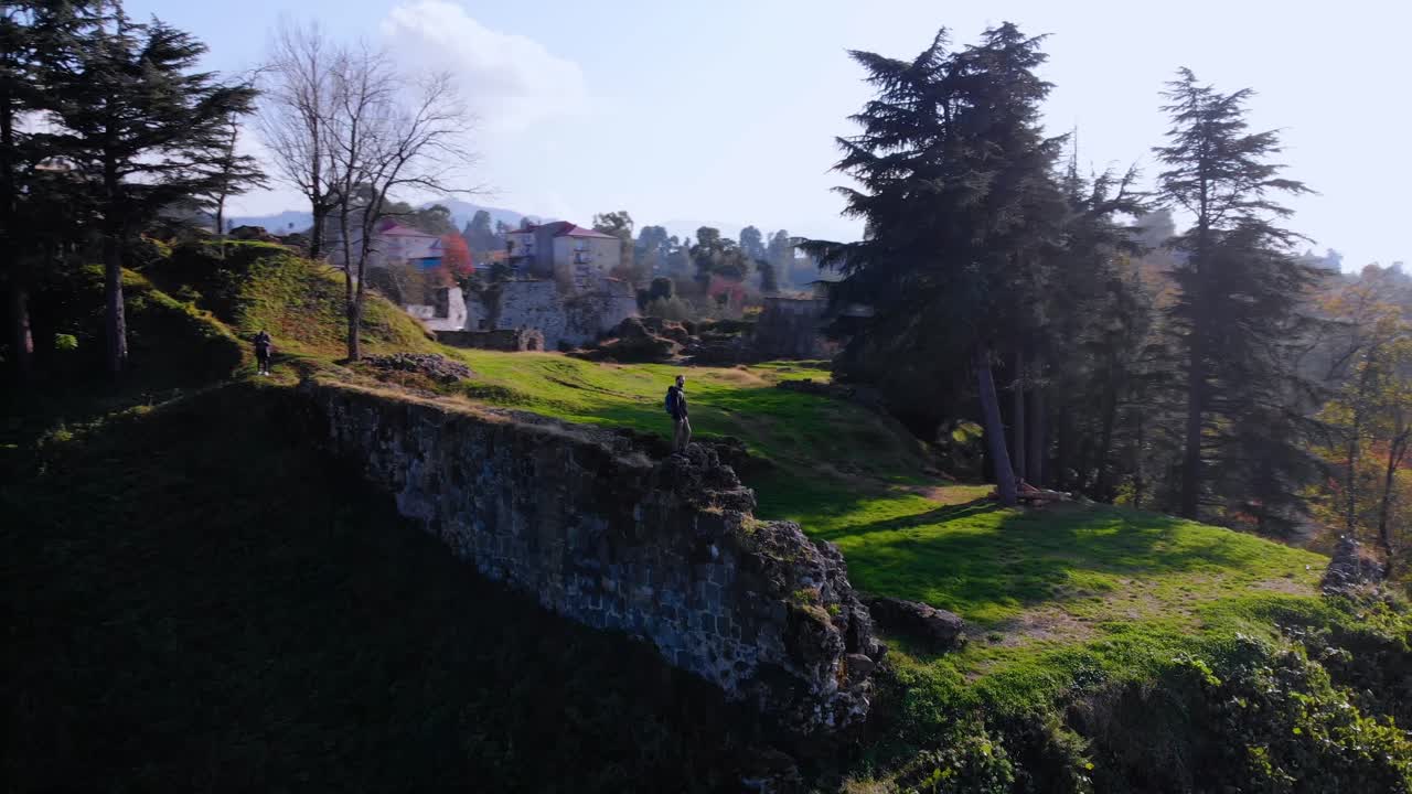 Aerial, orbit, drone shot, of a man standing on the ruins of the Petra fortress, during golden hour, in Kobuleti, Adjara, Georgia