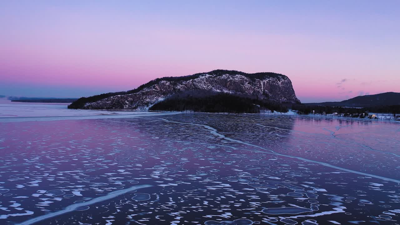 얼음에 선과 원의 패턴이 있는 새벽에 얼어붙은 호수 위의 멀리 떨어진 고립된 산 주위의 공중 궤도