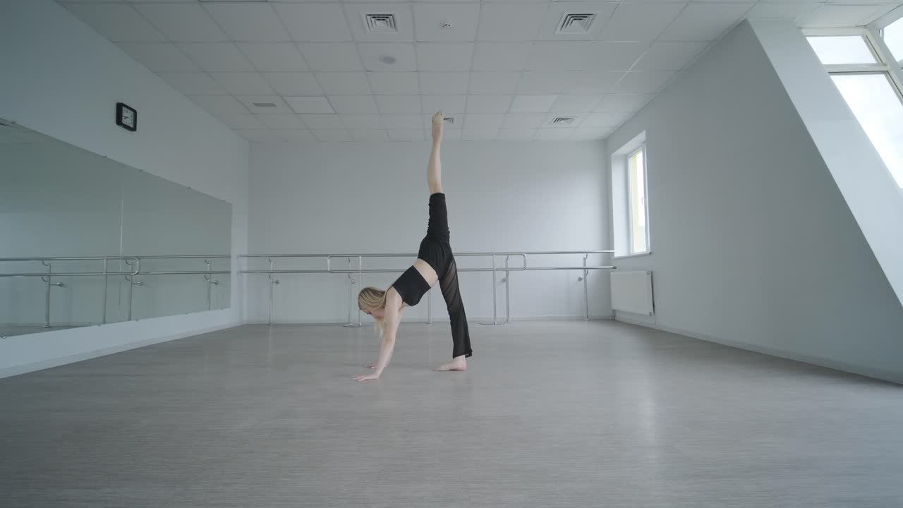 chica en forma con ropa negra actuando contemporáneamente. bailarina muestra movimientos fluidos, cuerpo y manos ondas en la habitación blanca. coreografía de danza de ballet moderno. joven se mueve suavemente
