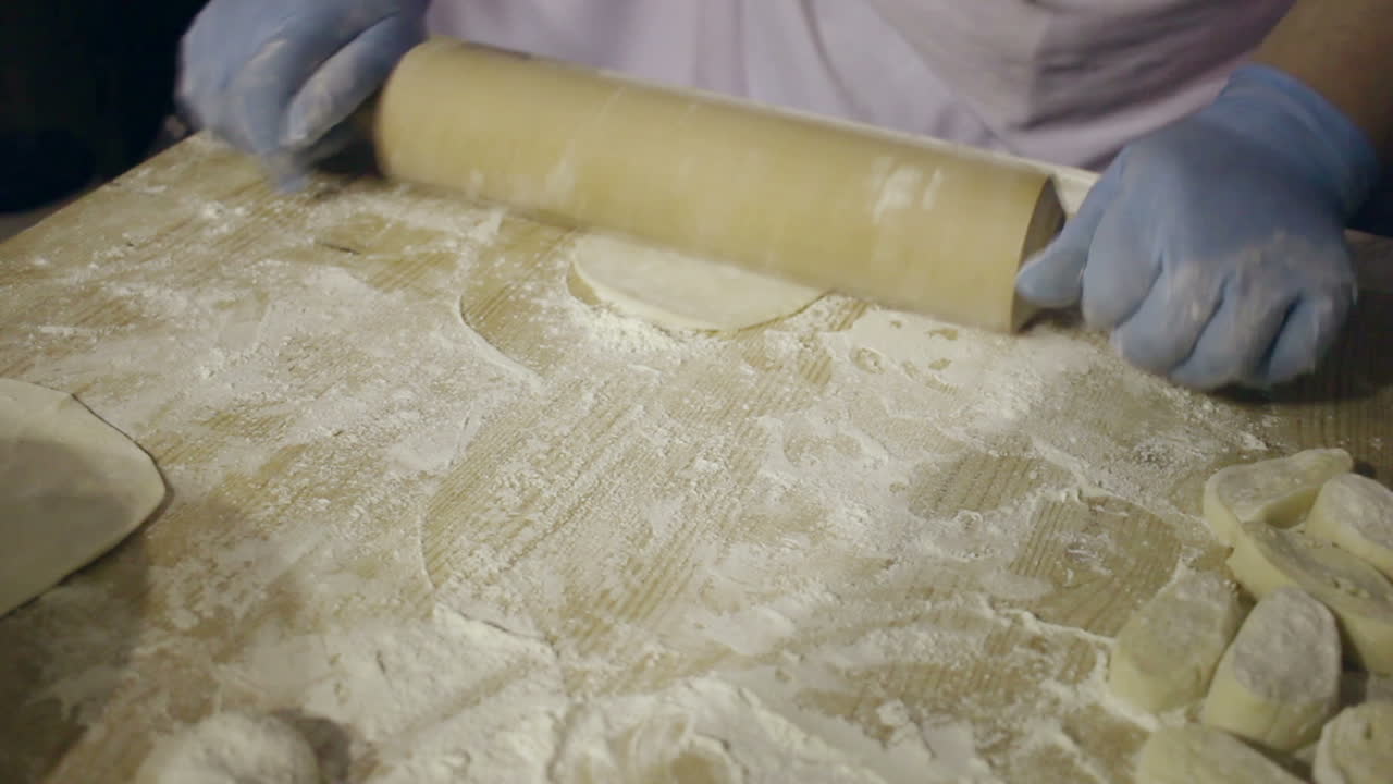 Stendere l'impasto con il mattarello. Mani dello chef che stendono una palla di impasto con il mattarello.