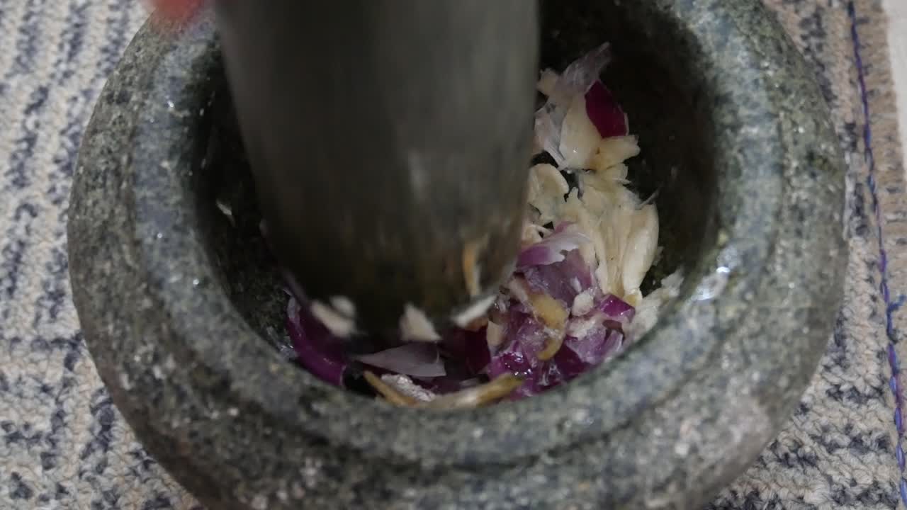 The ingredients for cooking are being solved manually by using a stone mortar and pestle. This method enhances the overall taste of the ingredients.