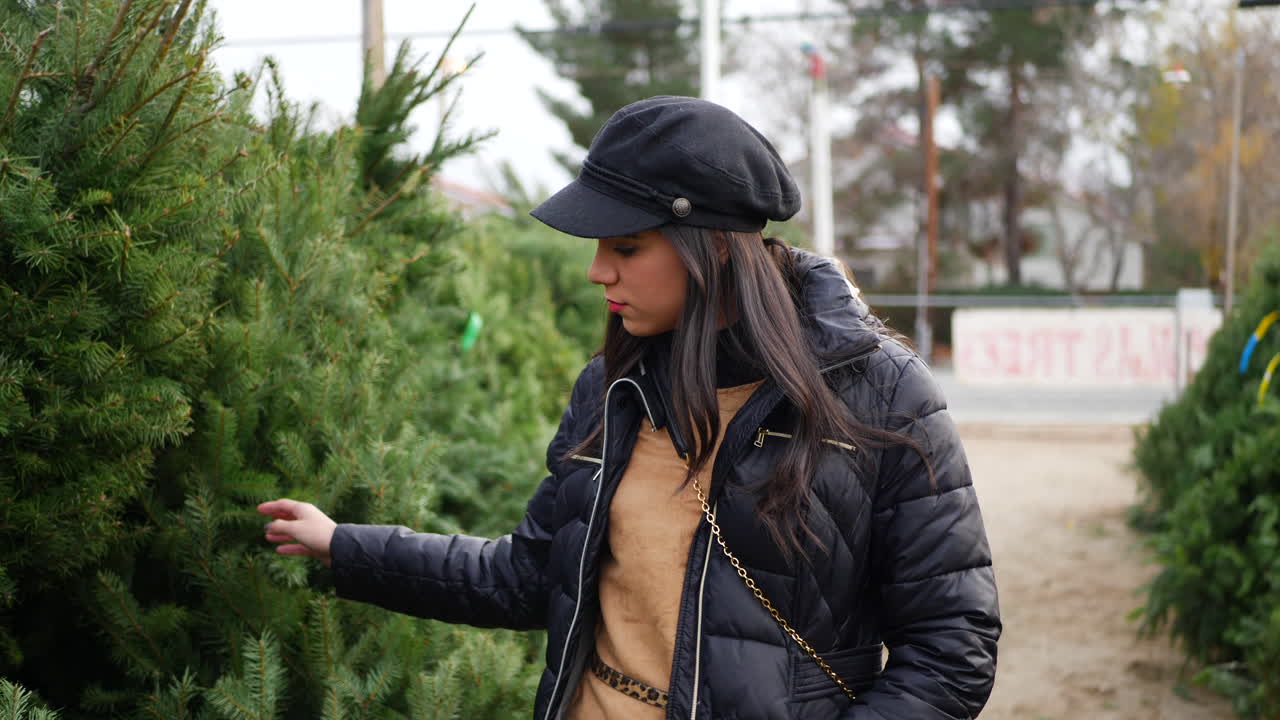 испаноязычная женщина покупает сезонную рождественскую елку на участке с множеством видов праздничных деревьев