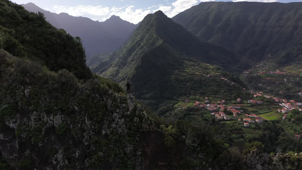 disparo de un dron circular de un hombre parado en una pose de héroe poderoso y confiado en el borde de la montaña con vistas al hermoso paisaje de madeira