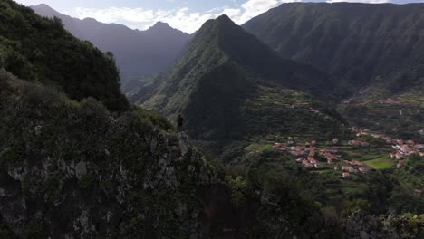 Circling-drone-shot-of-a-man-standing-in-a-powerful-and-confident-hero-pose-on-the-edge-of-the-mountain-overlooking-the-beautiful-scenery-of-Madeira