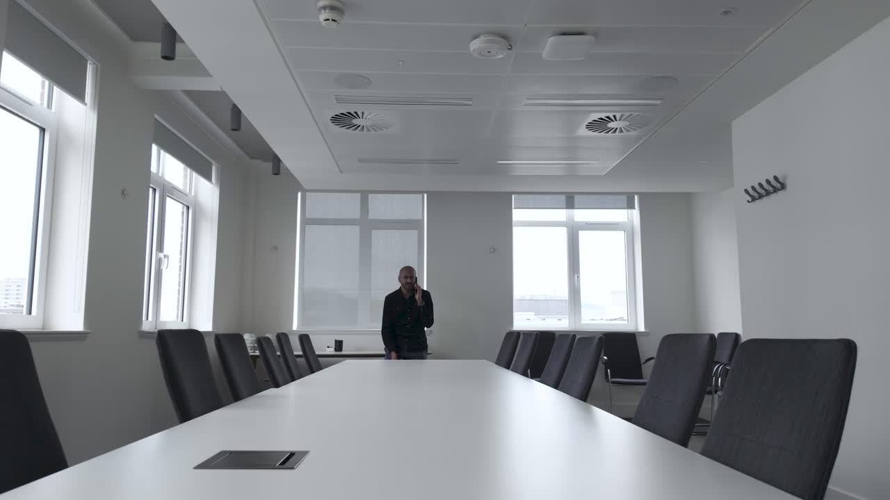 Male Sat And End Of Long Boardroom Table In Empty Conference Room Speaking On Mobile Phone