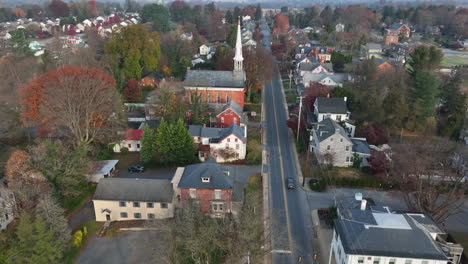 aerial tracking shot of traffic driving through small town in usa during autumn fall season past beautiful red brick church with white steeple