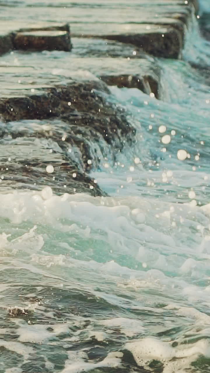 sea waves are washing the rocks near the shore during the day. Slow motion. Vertical video