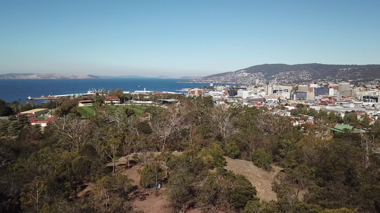 panorámica aérea sobre los árboles para revelar el puerto costero y la ciudad de hobart, tasmania, australia