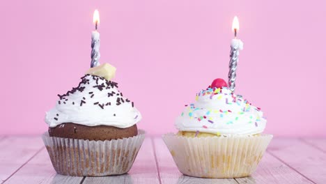 two testy sweet cup cakes with cream and burning candles on the table