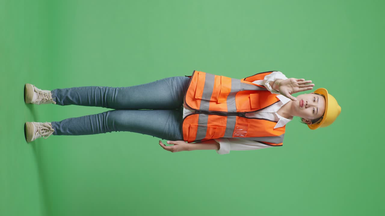 Full Body Of Asian Female Engineer With Safety Helmet Disapproving With No Hand Sign While Standing In The Green Screen Background Studio
