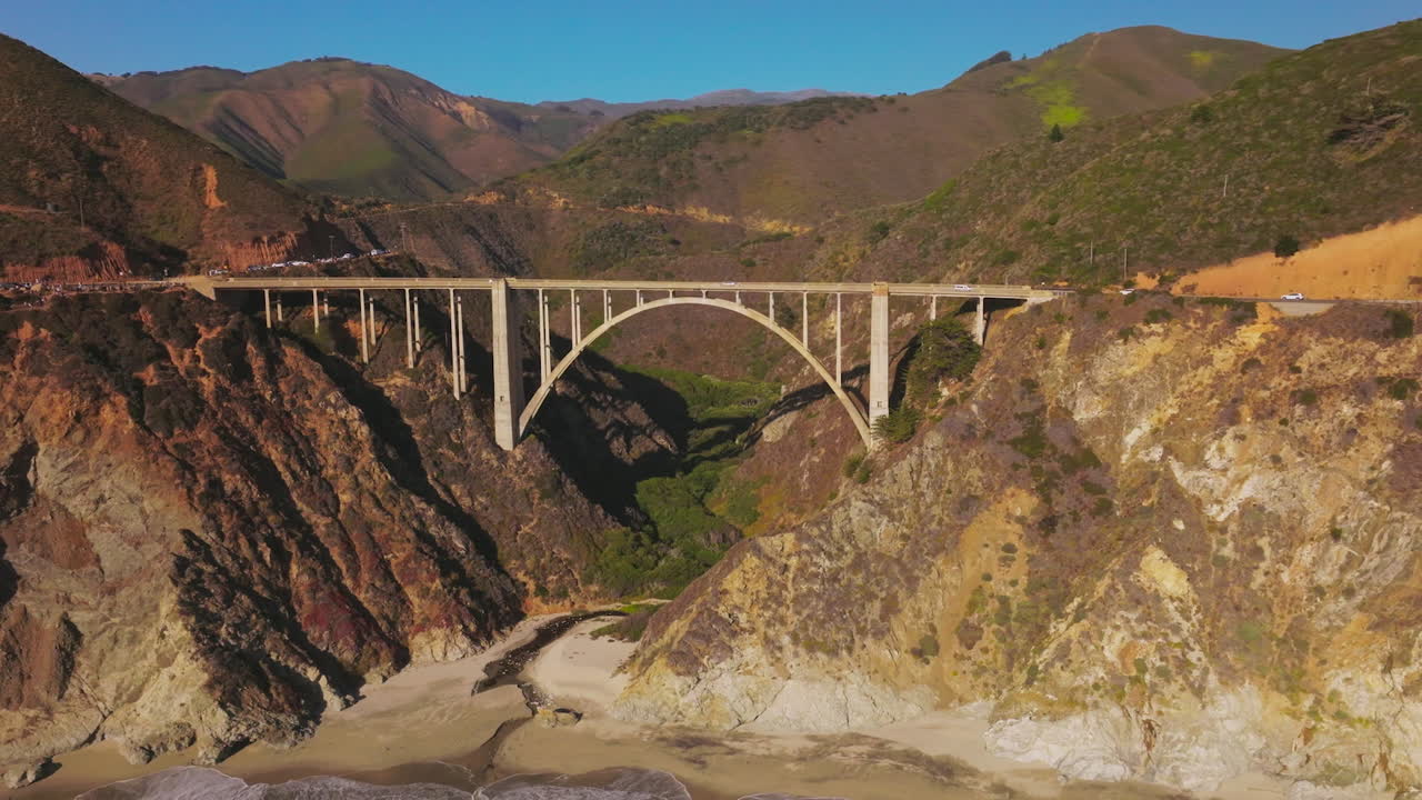 Arched bridge over the gap between the mountains. Sunlit mountains of California in the bright rays of sun. Aerial perspective.