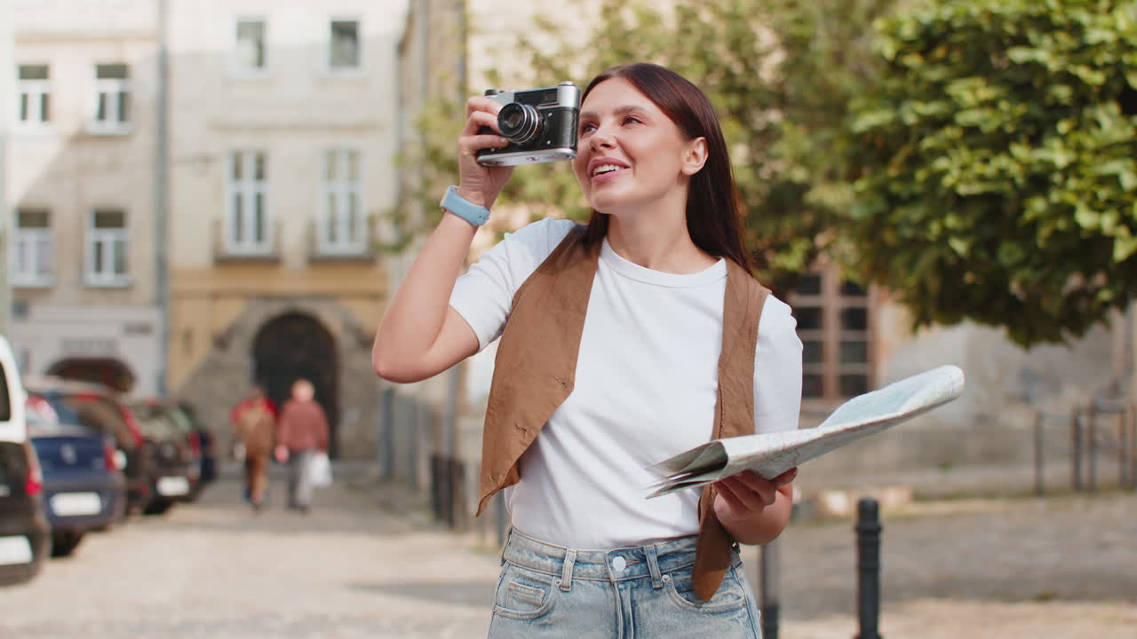 행복한 젊은 여성 여행자 관광객이 지도를 들고 도시 거리에서 레트로 카메라를 사용하여 사진을 찍습니다.