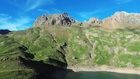 aerial footage of valle de ip near canfranc, spain, showcasing majestic green mountains and a tranquil lake under a vibrant blue sky. captures nature's serenity and rugged beauty