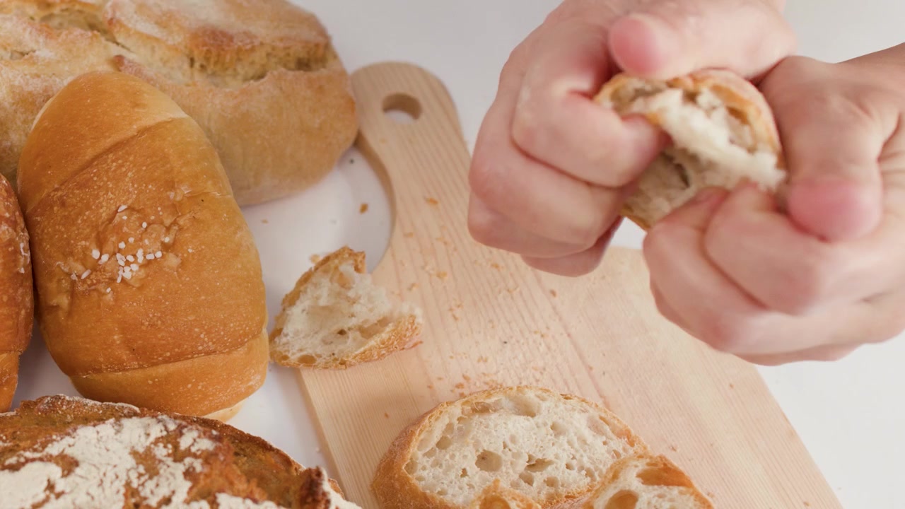 Close-up of hands tearing artisanal sourdough bread over a wooden board with bright lighting.