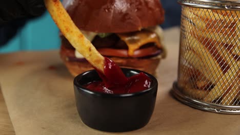 hand dipping french fries into ketchup next to burger and fries basket