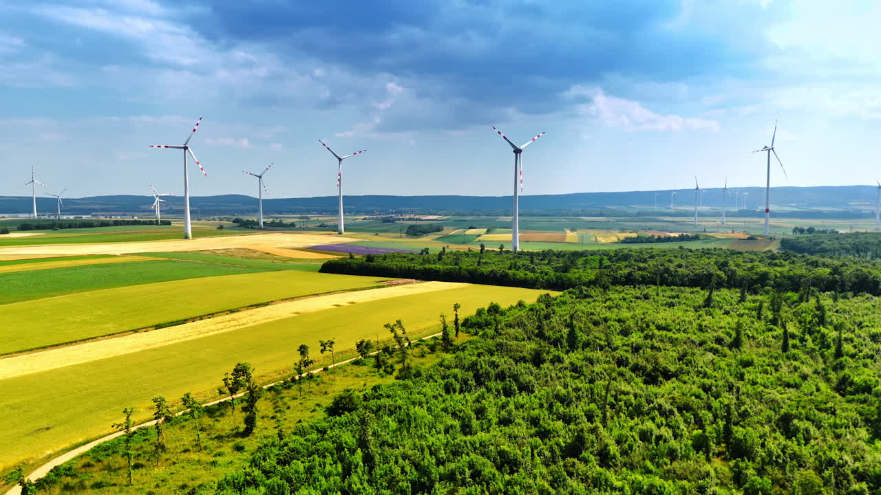 Turbines rise in a green field. Wind turbines rise above green fields and forests, highlighting renewable energy in a vibrant rural area