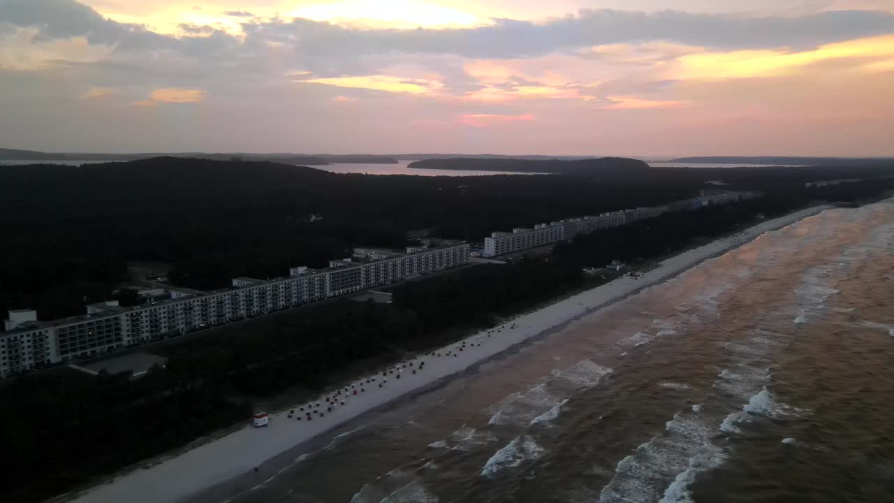 Golden sunset over the historic Prora complex in Rügen, with waves gently rolling onto the sandy shoreline.