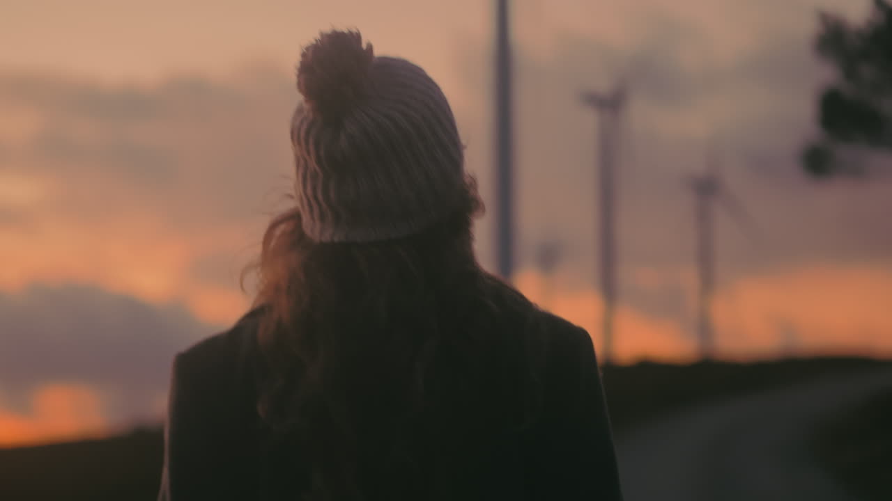 Blonde Caucasian young woman walks in Portugal, admiring stunning natural scenery on a windy day. Cinematic shot captures her savoring the sunset landscape. Promotes enjoyment of nature and travel.