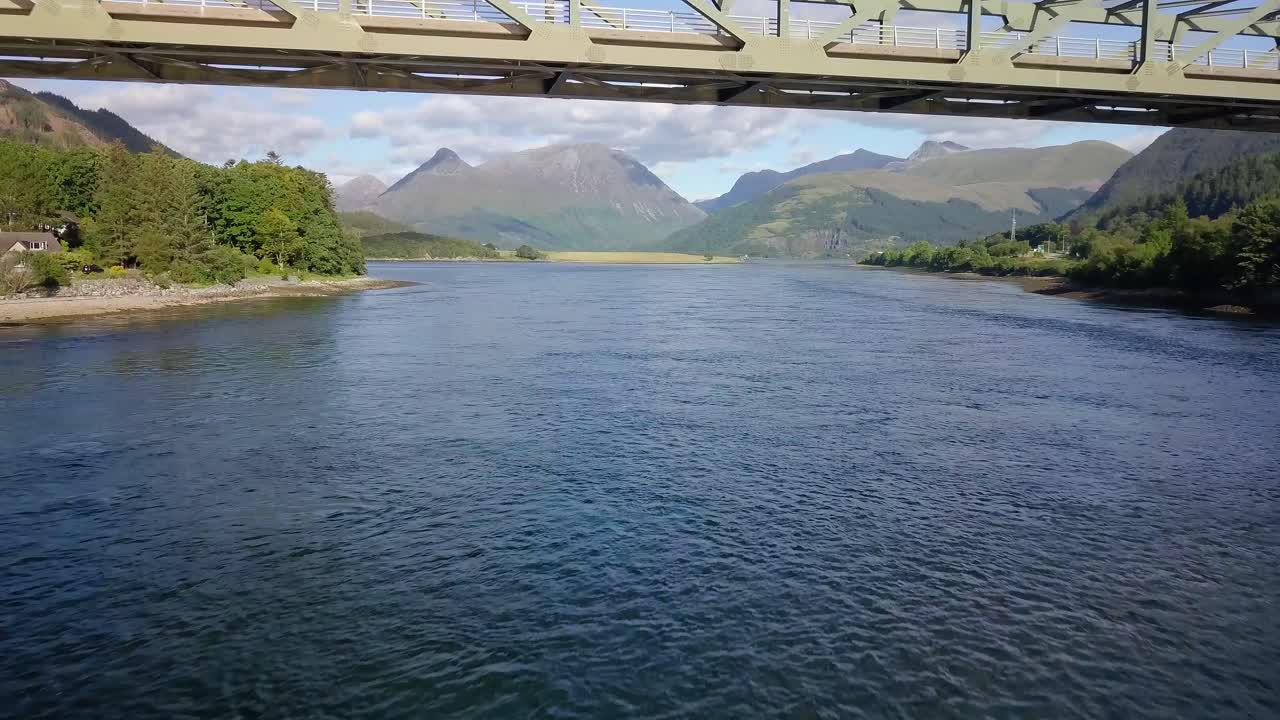 Aerial shot of flying under a bridge and then going higher to reveal the background. Some vehicles drive over the bridge as the camera gets higher.