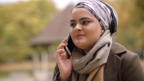 british muslim woman using mobile phone in park