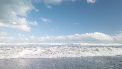 slowmo ocean wave rolls in to camera with picturesque cloudy sky