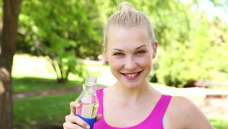 una rubia en forma bebiendo agua en el parque.