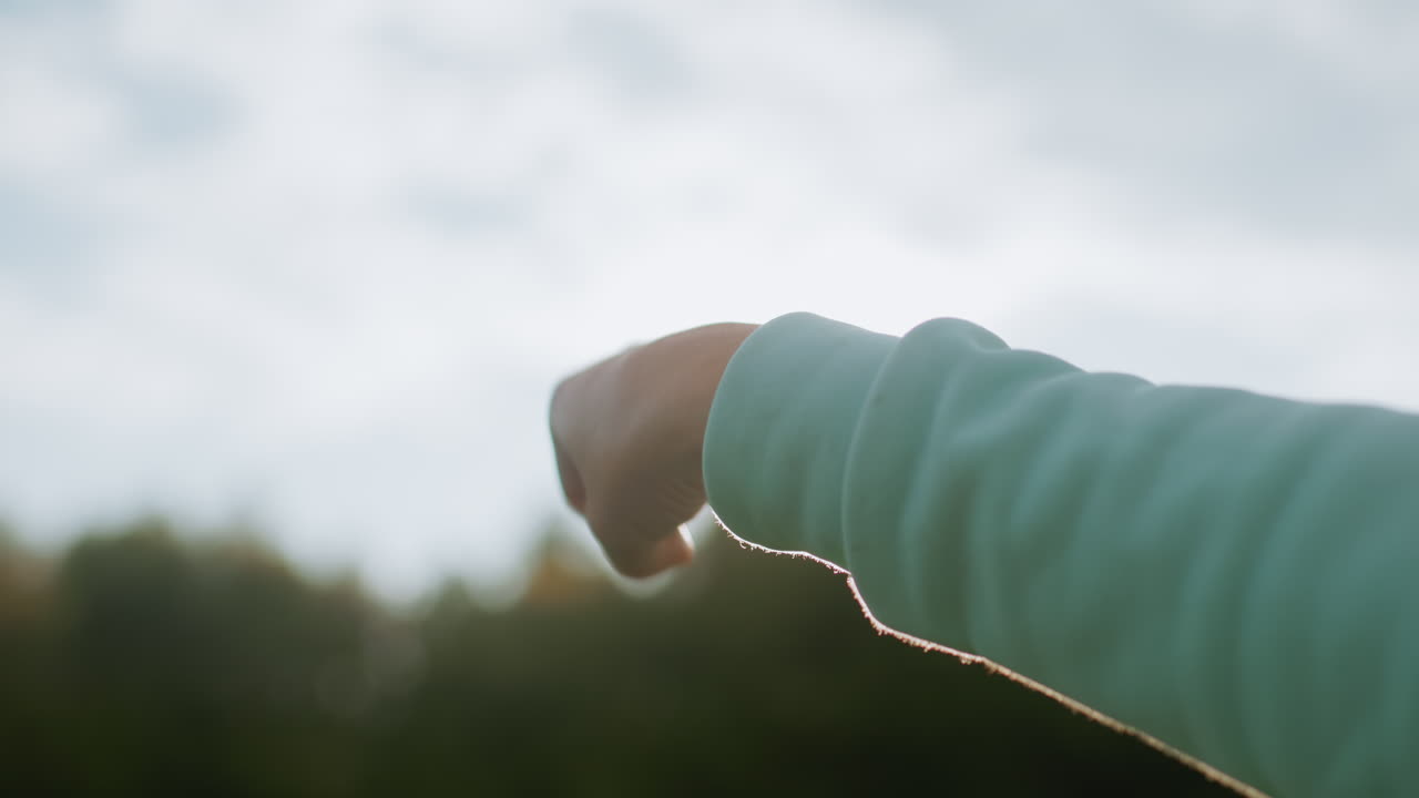 Close up of female hand in mint green sleeve performing hand rotation exercise outdoors during peaceful morning session in open grassy field under soft natural light surrounded by fresh green trees