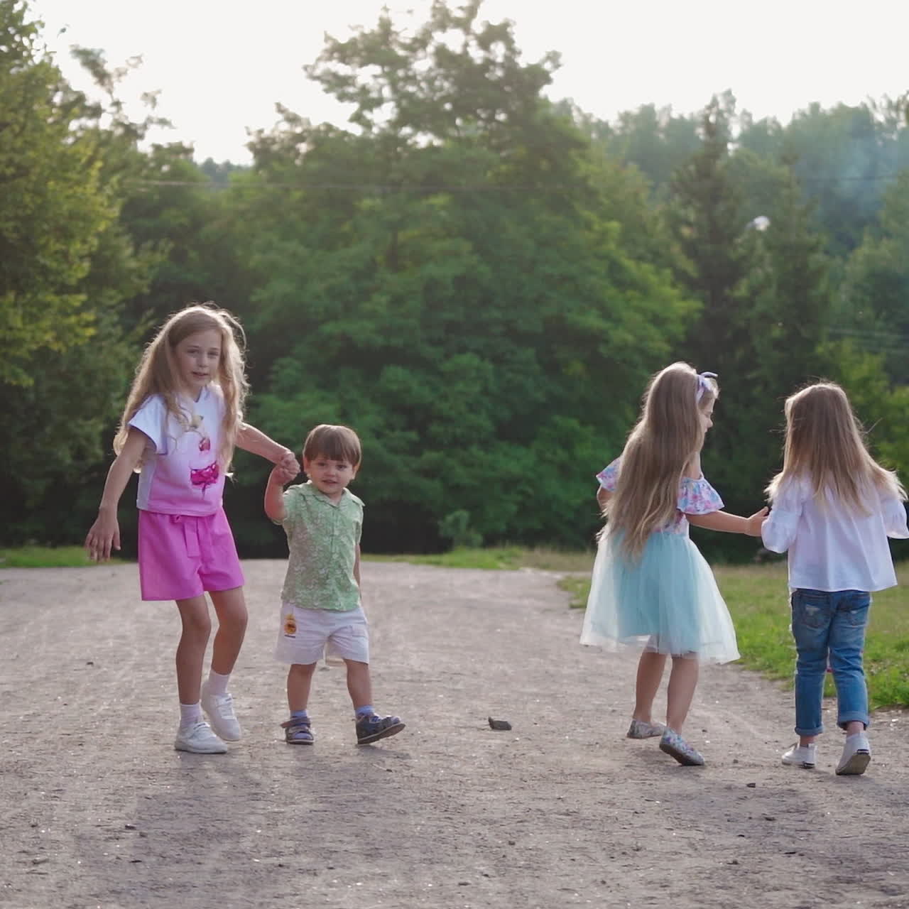 Joyful children on the background of green trees in summer. Girls and little boy walking merrily in the park. Happy childhood.