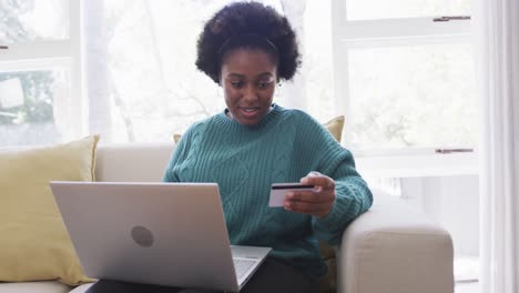 happy african american woman making payment using credit card and laptop at home, slow motion