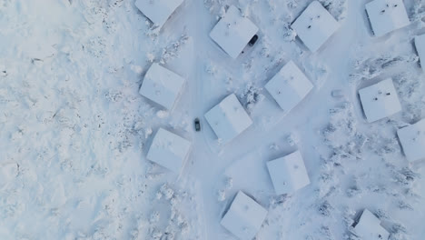 tomada aérea de las aves siguiendo el coche que conduce entre las cabañas nevadas de laplandia