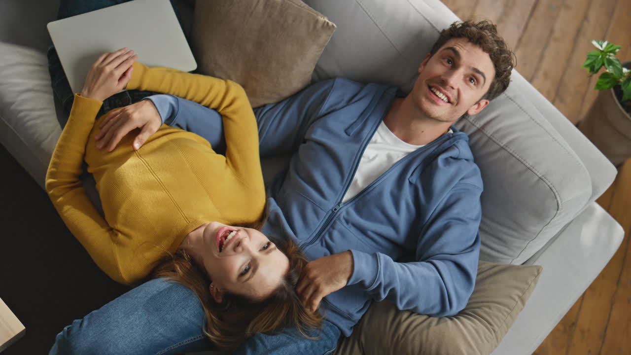 Laughing sweethearts relaxing sofa at new house top view closeup. Pair enjoying