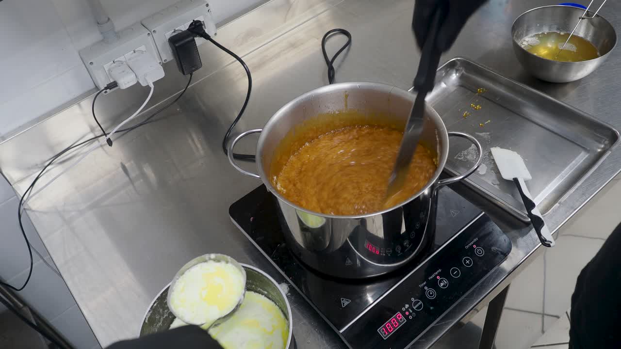 chef cooking salted butter caramel dessert , boiling, styr with spatula, hot smooth cooked salty sauce in steel pan on stove