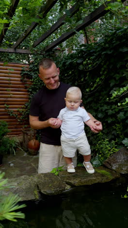 caucasian father shows his little baby a fountain. cute blond baby boy in white clothes looks at water with interest. vertical video.