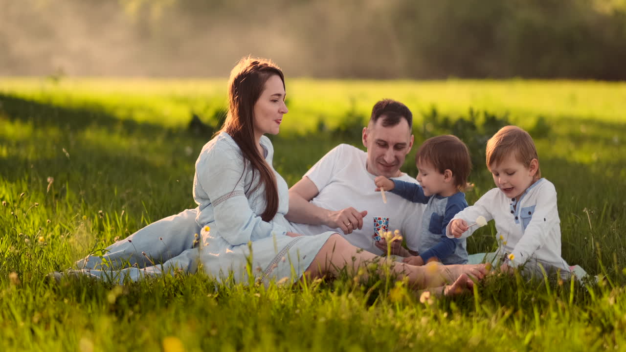 I bambini danno da mangiare alla mamma il gelato durante un picnic, un pranzo in famiglia all'aperto nel campo in mezzo alla natura.