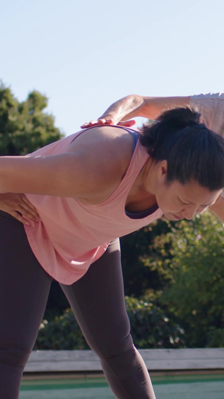 Vertical video: Placing guiding hand, coach helping woman in pink top aligning posture on pool deck
