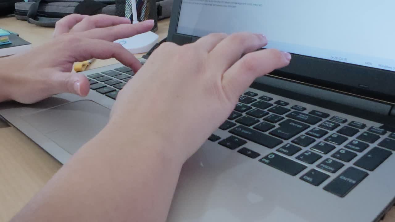 Person's hands engaged in typing on a laptop at a home office desk