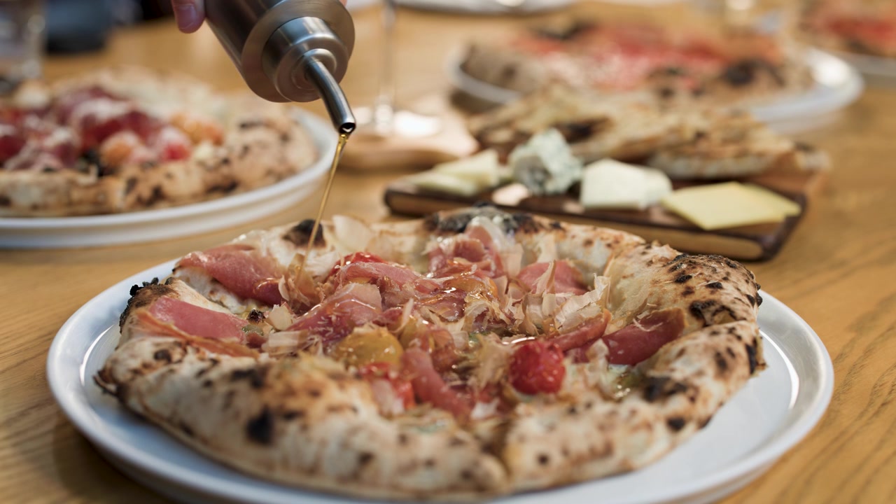 Primo piano di olio d'oliva versato su pizza artigianale cotta nel forno a legna in un luminoso ristorante italiano