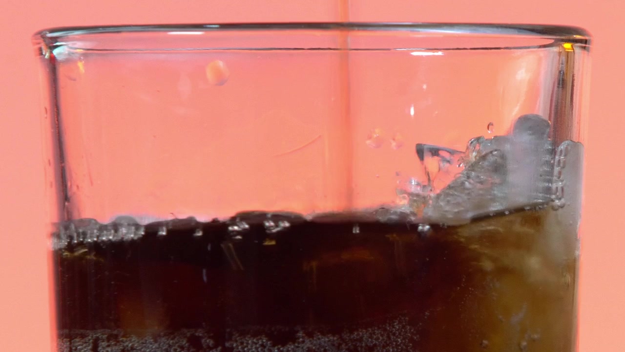Bibita gassata versata in un bicchiere pieno di cubetti di ghiaccio, che cattura lo schizzo rinfrescante e le bollicine di carbonatazione