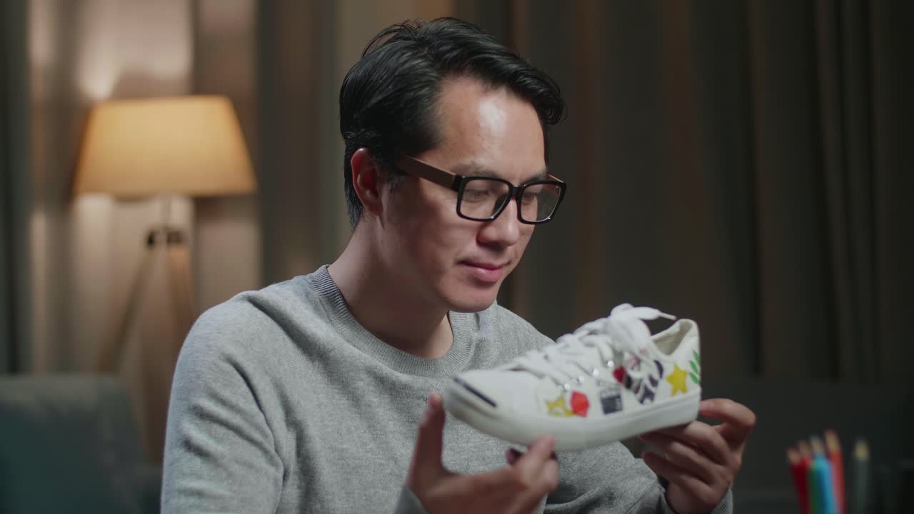 아시아 남성 신발 디자이너가 집에서 데스크 컴퓨터에서 작업하는 동안 카메라에 미소 짓고 있습니다.