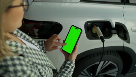 mujer usando el teléfono para cargar un vehículo eléctrico