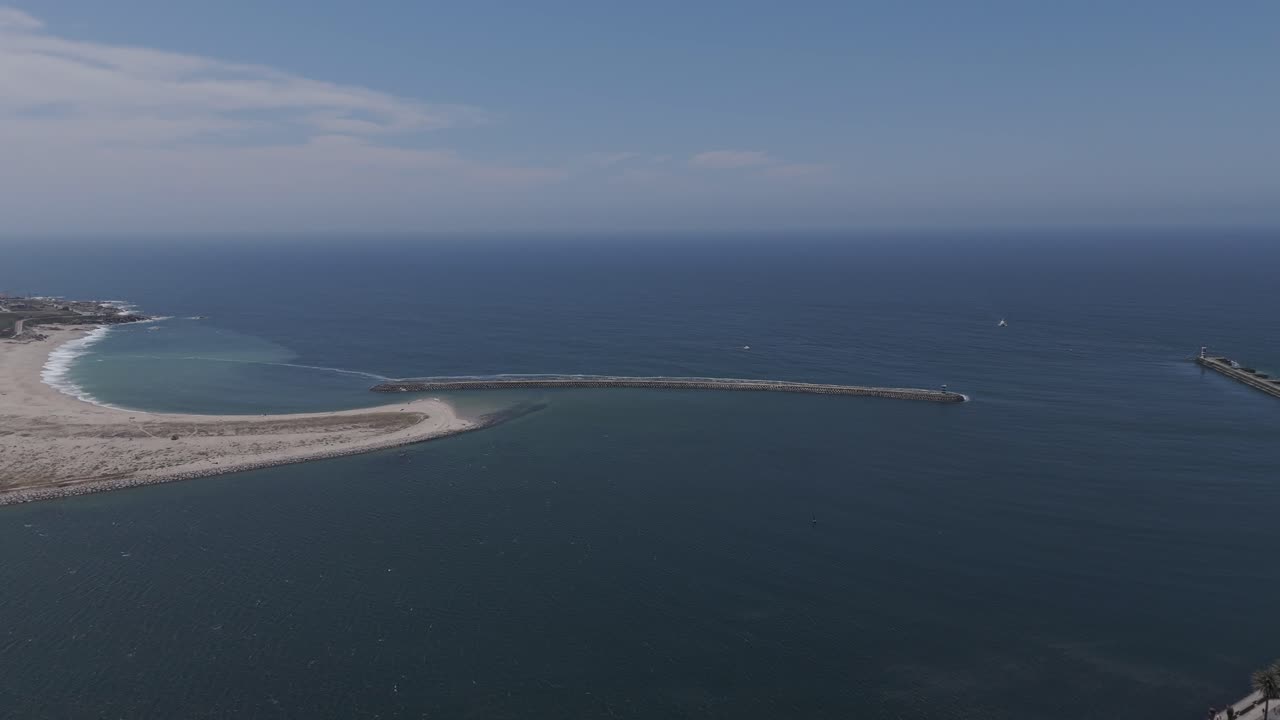 aerial rotation of foz do porto portugal with curved sandy beach and stone pier meeting ocean