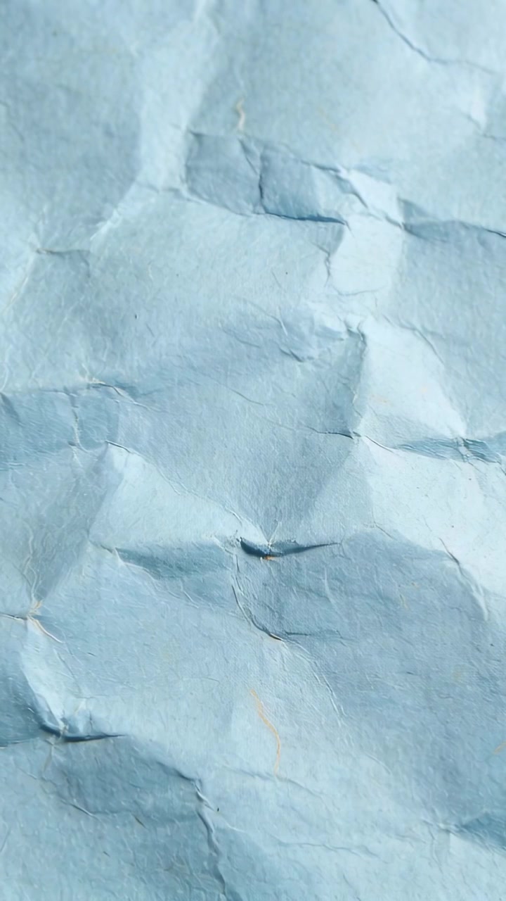 Vertical video: Filming crumpled light-blue paper resting on table, showing folds and small smudge
