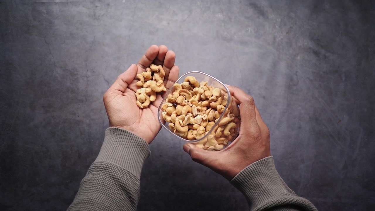 Person Pouring Cashew Nuts from a Container into Hand
