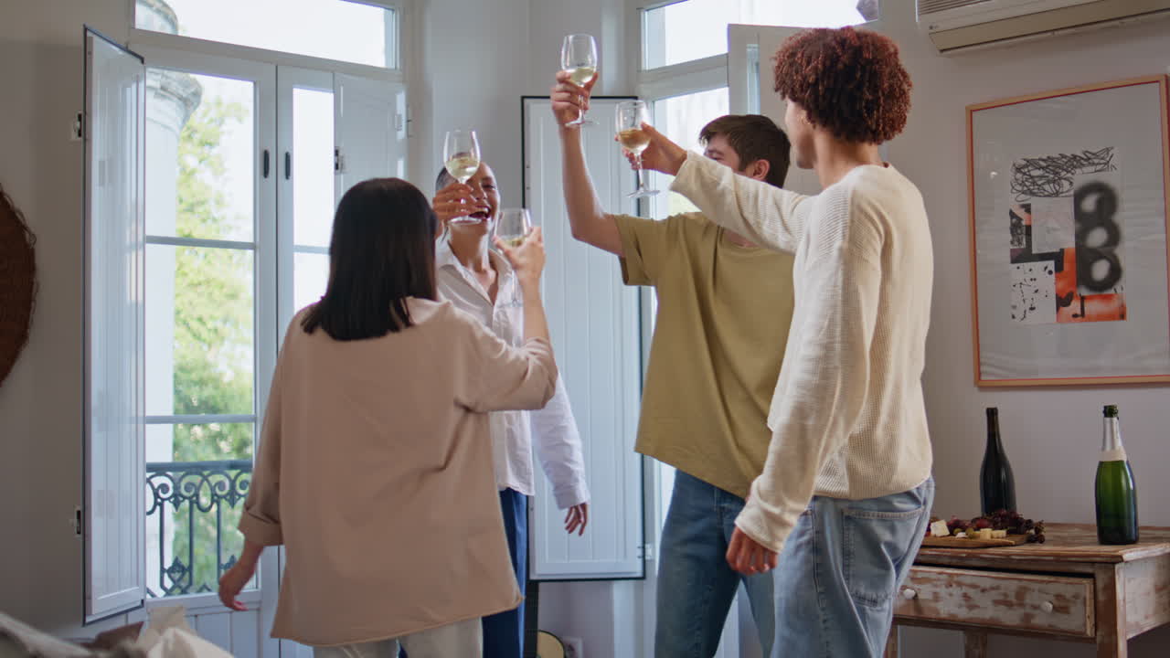 Company clinking wine glasses having fun house party. Overjoyed friends dancing