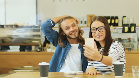 caucasian man and woman friends making a video call using smartphone sitting at a table in a cafe