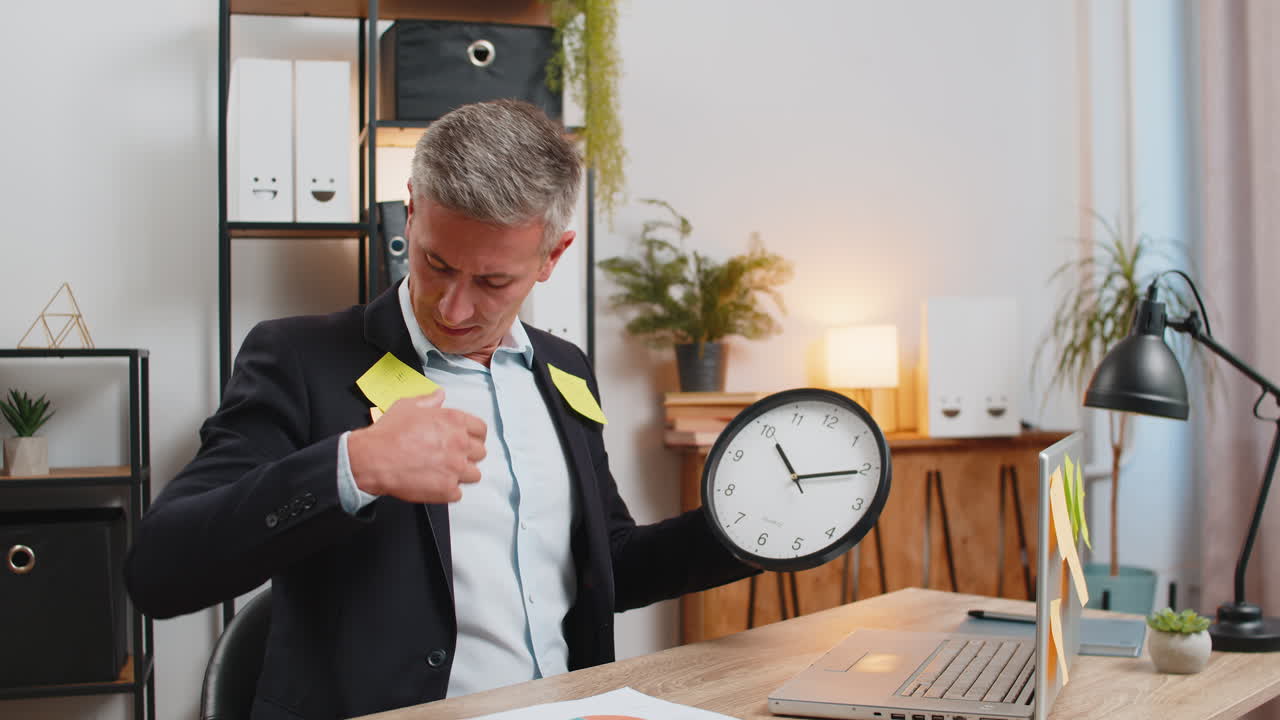 Frustrated young businessman in formal suit with clock and sticky notes sitting at home office desk