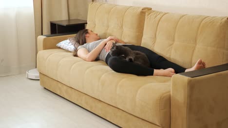 woman sleeps on sofa cat looks at robot cleaner at home