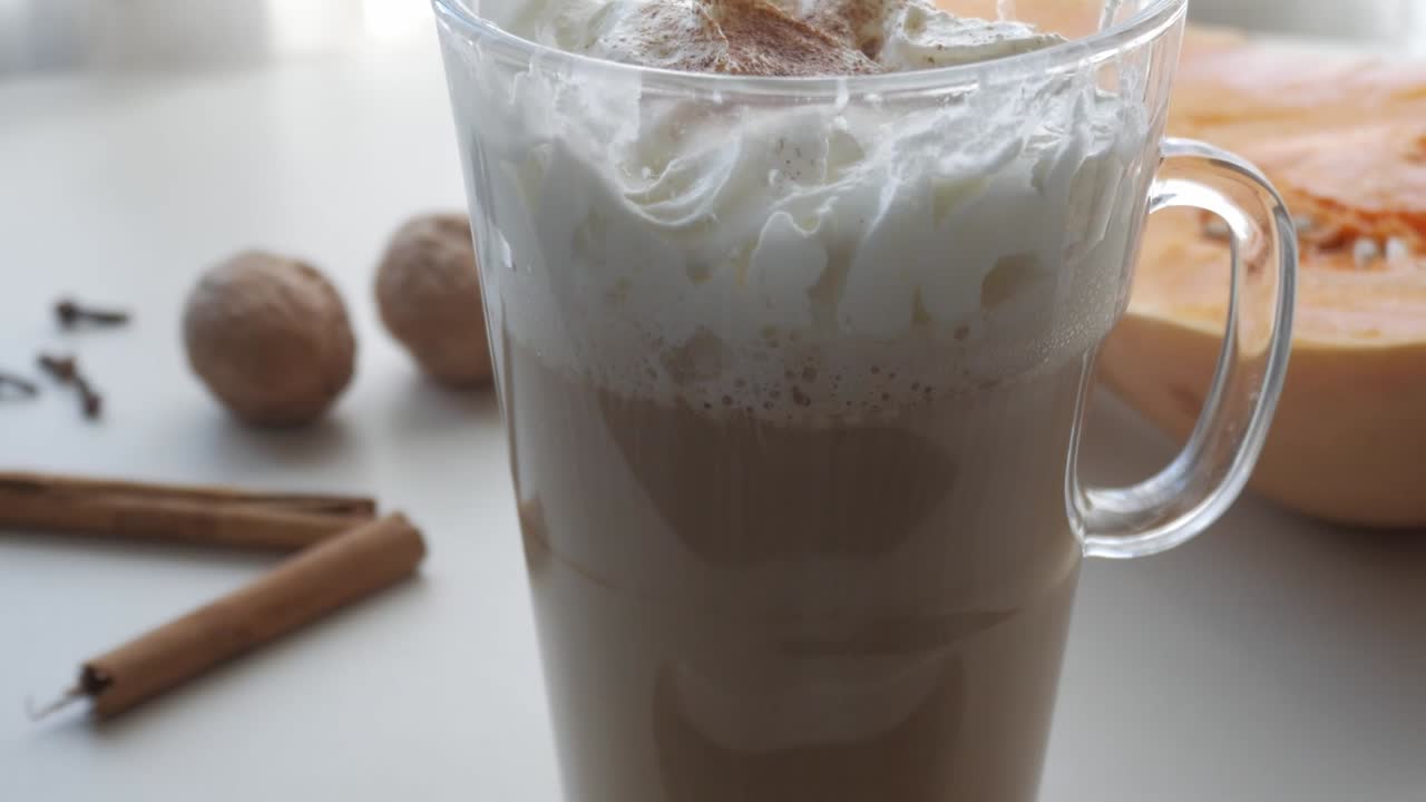 Zoom inn på en klar, høy glasskopp med kaffe eller kakao med krem, kanel, gresskar, nøtter og nellik. Julearomaer.