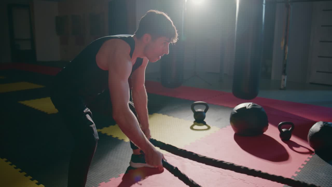 Ung mann som trener med battle ropes i et mørkt treningsstudio