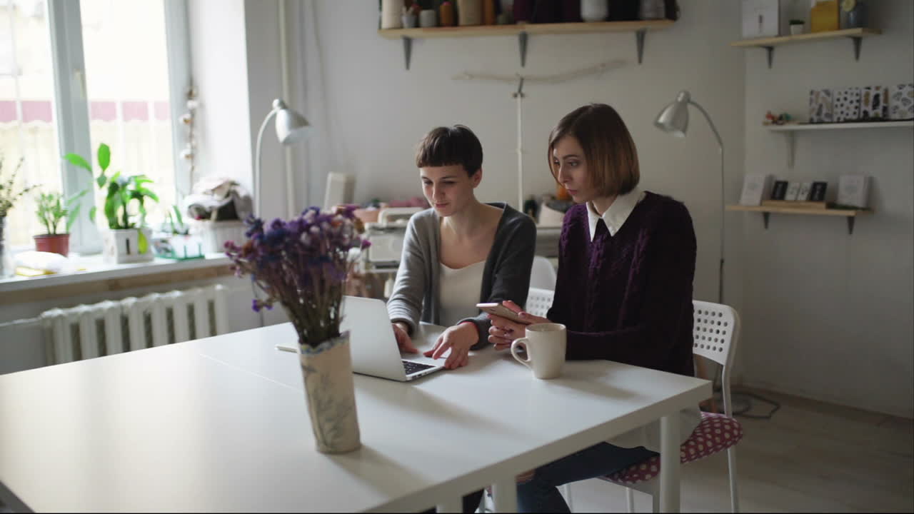 Two young woman sitting at table and using notebook for order online